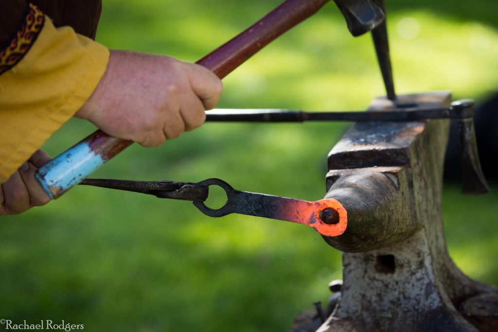 A blacksmith working on a bottle opener at an anvil